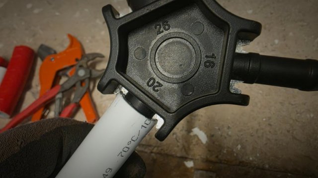 Hand in Arbeitshandschuh kalibriert ein wei&szlig;es Kunststoffverbundrohr mit einem sternf&ouml;rmigen Mehrfach-Kalibrierdorn.