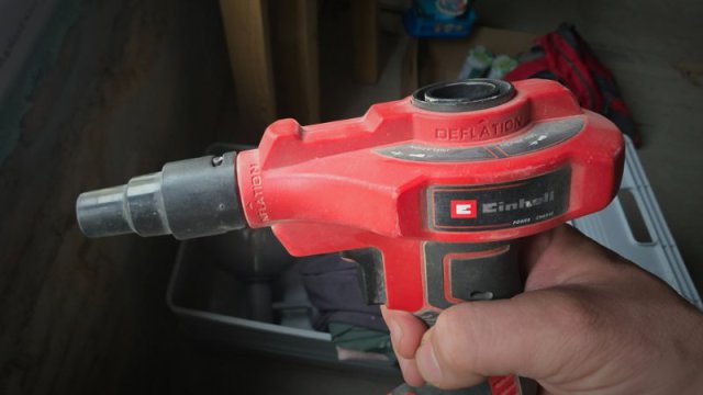 Rote Einhell Akku-Luftpumpe CE-AP 18 Li mit schwarzem Aufsatz in einer Hand gehalten, bereit f&uuml;r den Baustelleneinsatz.